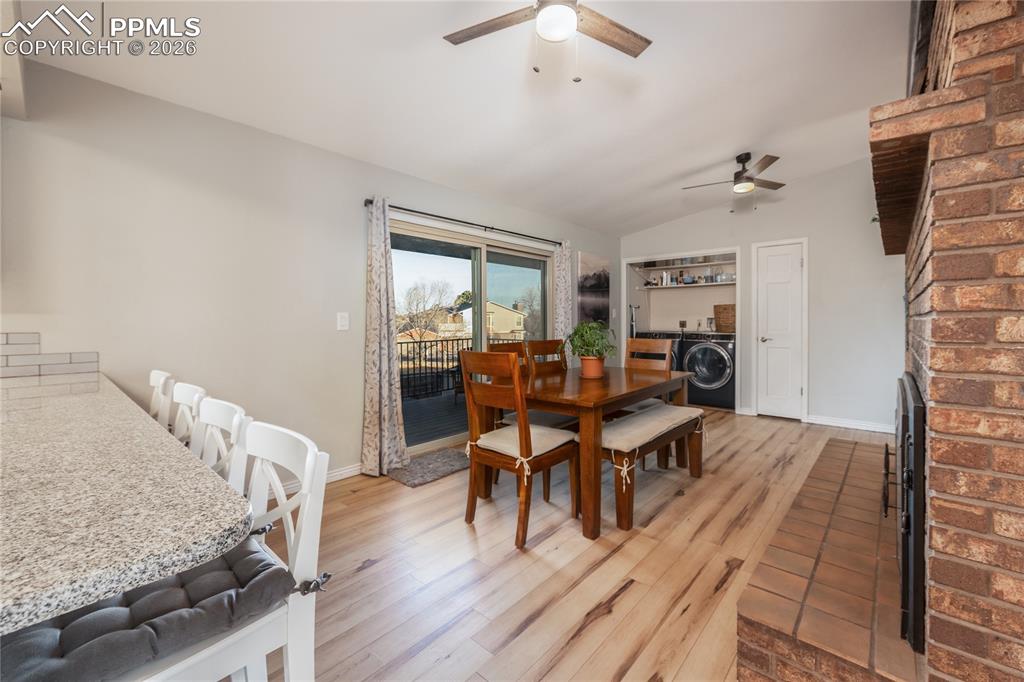 Dining room featuring light wood-style flooring, a brick fireplace, lofted ceiling, and ceiling fan