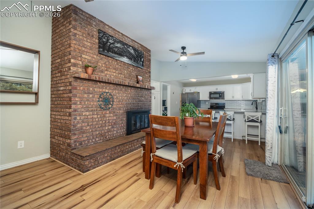 Dining area featuring ceiling fan, lofted ceiling, a brick fireplace, and light wood finished floors