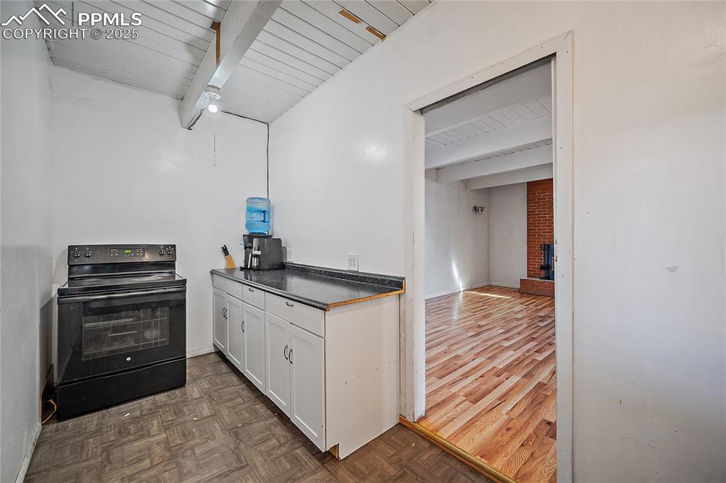 Kitchen featuring black electric range, white cabinetry, parquet floors, dark countertops, and a wooden ceiling with exposed beams