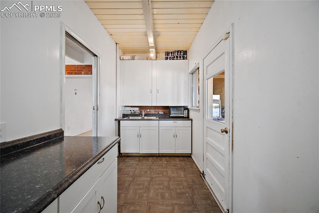 Kitchen with dark countertops, white cabinets, and beam ceiling