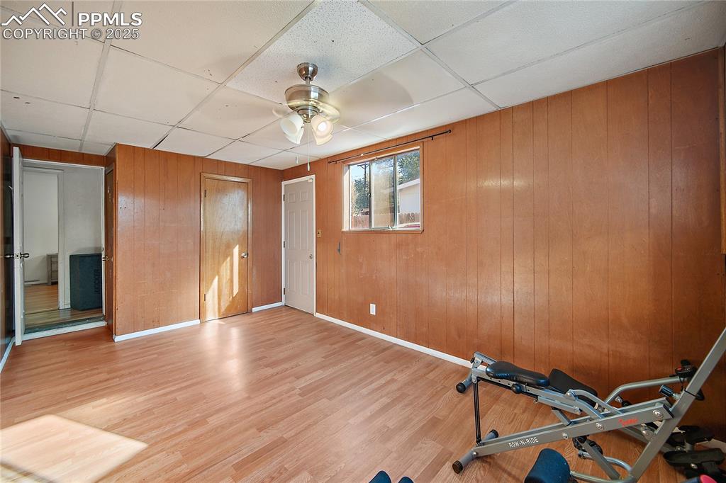 Workout room with wood walls, a paneled ceiling, wood finished floors, and a ceiling fan