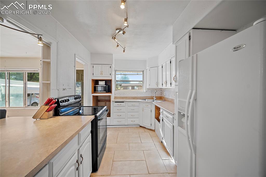 Kitchen with stove, refrigerator, white cabinetry, light countertops, and light tile patterned flooring