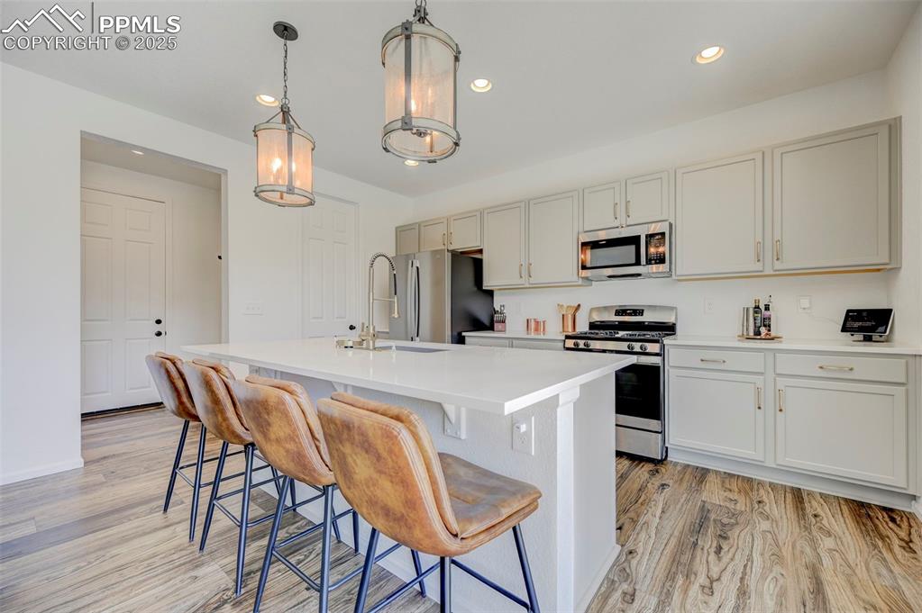 Kitchen with appliances with stainless steel finishes, light wood-style floors, a kitchen island with sink, light countertops, and a kitchen breakfast bar