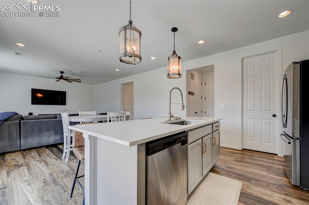 Kitchen with appliances with stainless steel finishes, ceiling fan, light wood finished floors, open floor plan, and a breakfast bar area