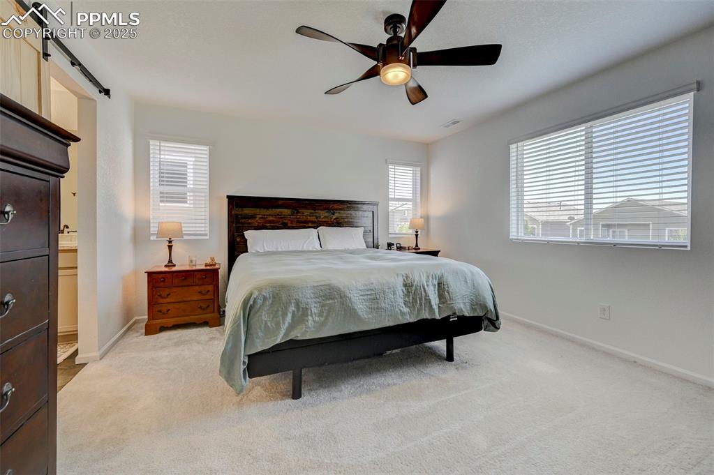 Bedroom with light colored carpet, a barn door, a ceiling fan, and ensuite bath