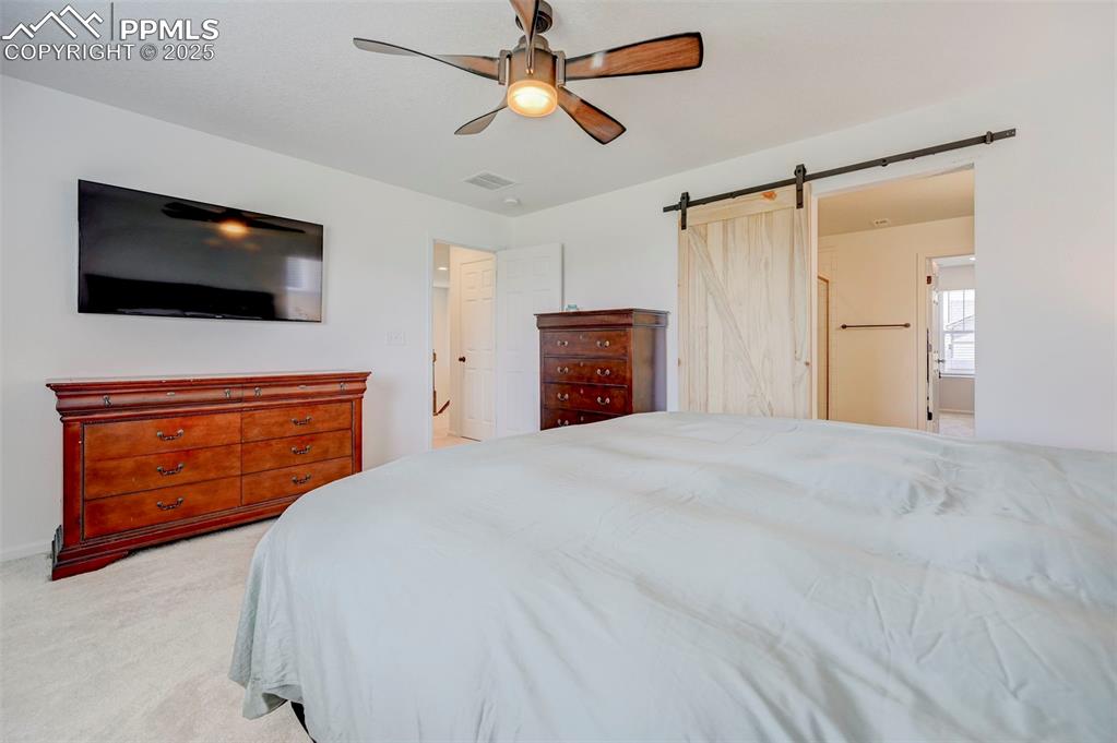 Bedroom with light colored carpet, a barn door, and a ceiling fan