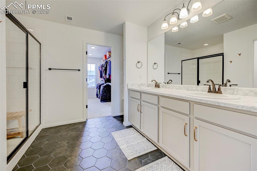 Full bath featuring a stall shower, double vanity, tile patterned floors, and a walk in closet