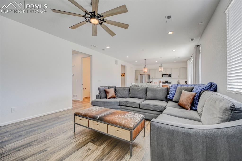 Living area with light wood-style flooring, ceiling fan, and recessed lighting