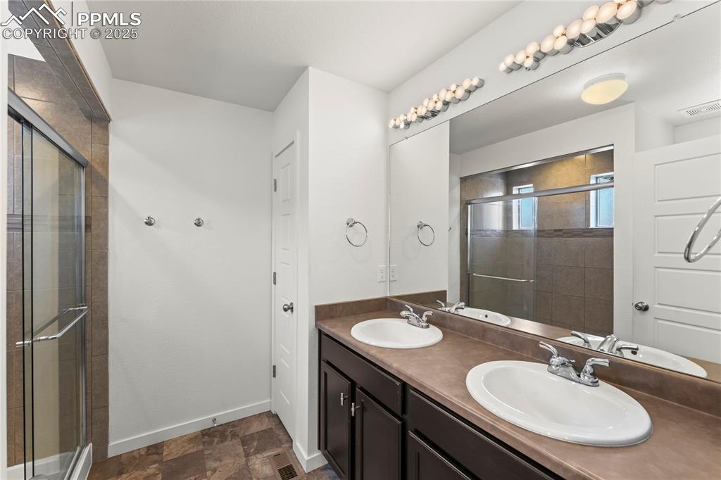 Bathroom featuring double vanity, stone finish flooring, and a stall shower