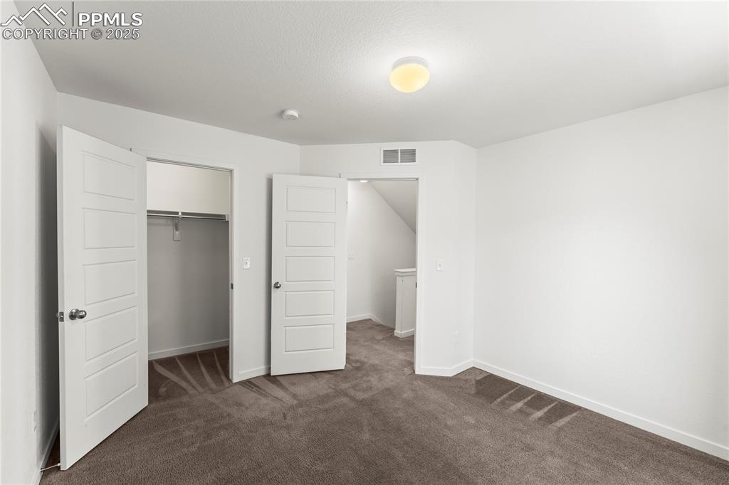 Unfurnished bedroom with dark colored carpet and a walk in closet