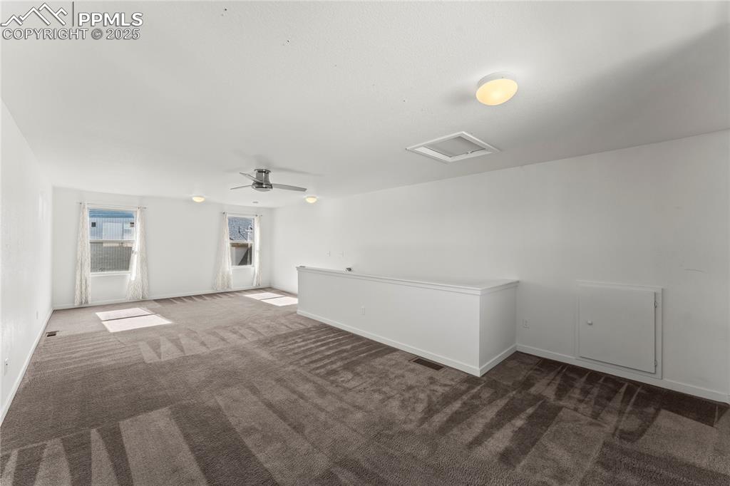 Empty room with dark colored carpet and a ceiling fan