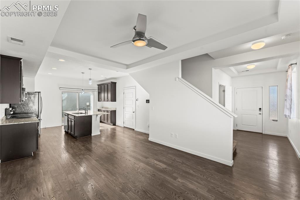 Unfurnished living room featuring dark wood-style floors, plenty of natural light, a ceiling fan, and a raised ceiling