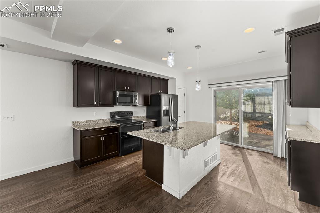 Kitchen with appliances with stainless steel finishes, light stone counters, dark wood-type flooring, dark brown cabinets, and decorative light fixtures