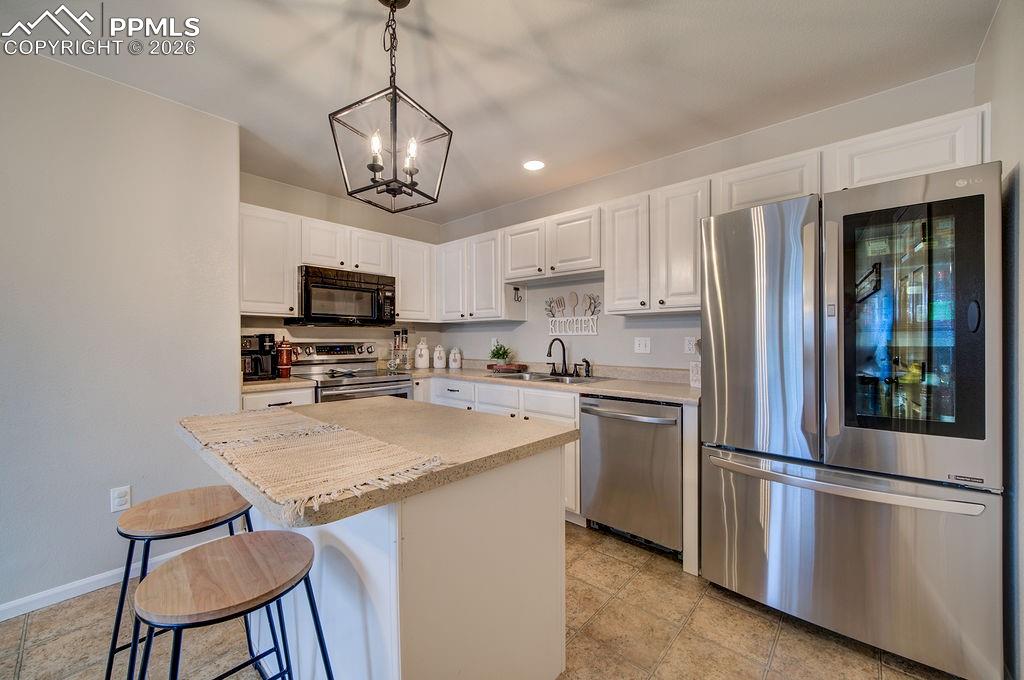 The Island Kitchen features a breakfast bar, white cabinets, modern light fixtures, stainless steel appliances, and solid countertops for easy food preparation.
