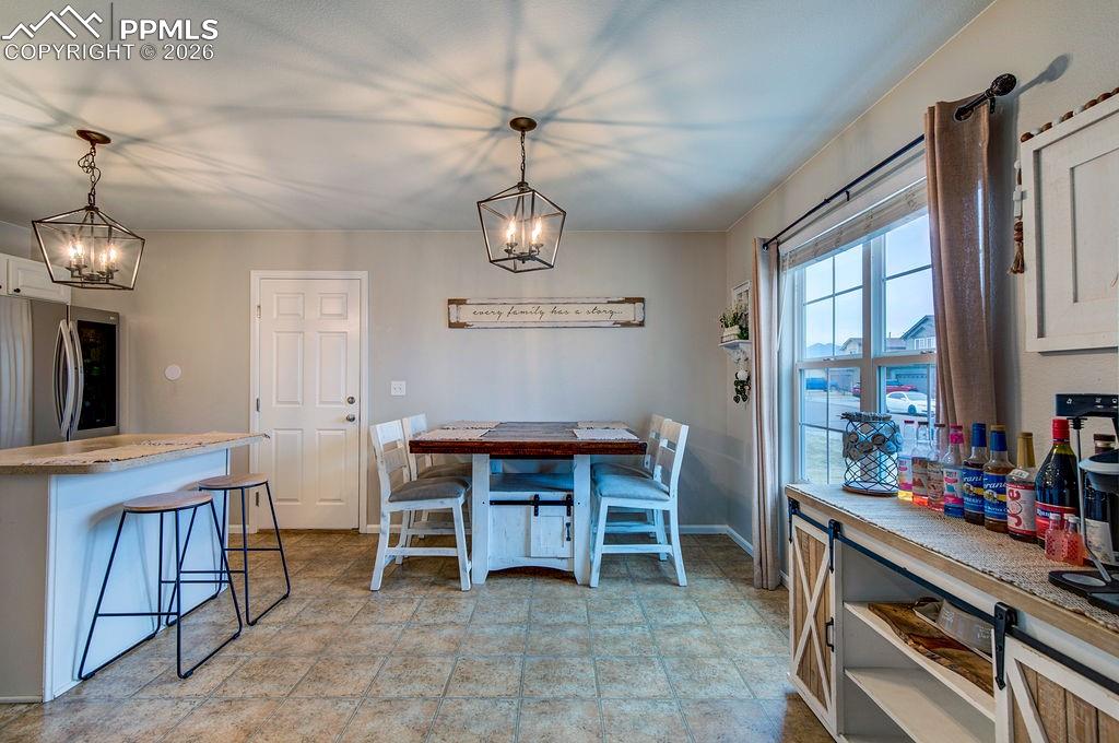 Light and bright Kitchen/Dining Area with vinyl flooring, a large view window with custom window treatments, modern light fixtures, and access to the 2-car attached garage.