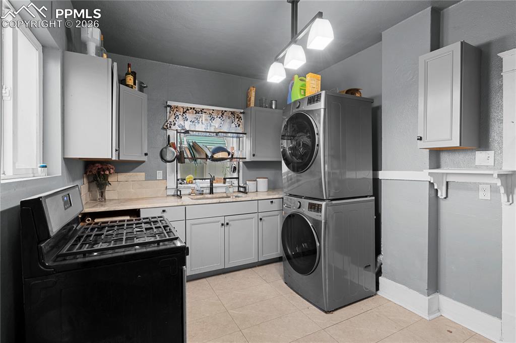 Kitchen featuring gas range oven, light countertops, pendant lighting, stacked washing machine and dryer, and light tile patterned flooring
