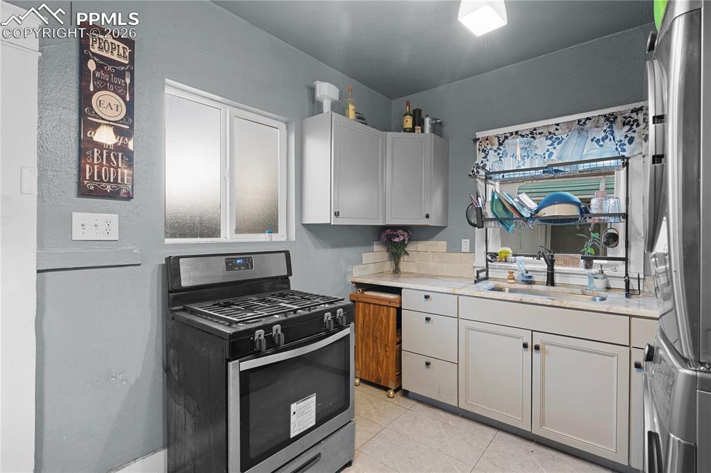 Kitchen featuring stainless steel appliances, light tile patterned floors, and stacked washing machine and dryer