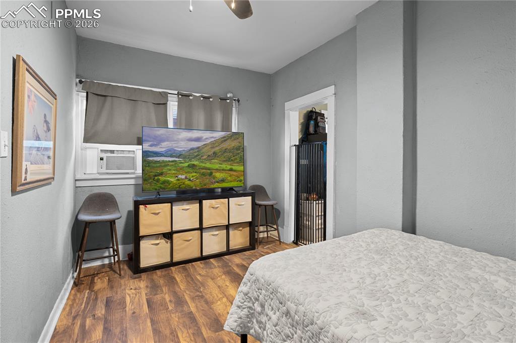 Bedroom with dark wood finished floors, a textured wall, ceiling fan, and cooling unit