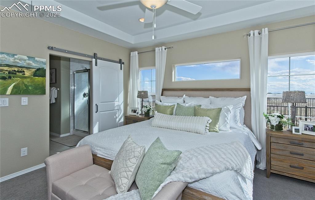 Bedroom with a barn door, carpet, ensuite bath, ceiling fan, and a raised ceiling