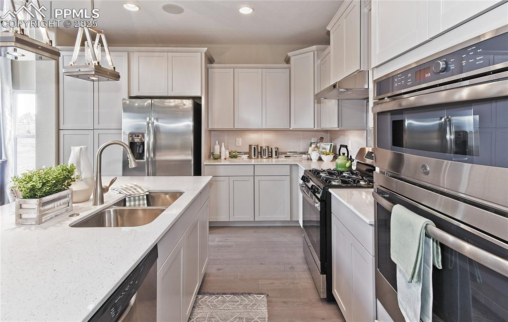 Kitchen featuring appliances with stainless steel finishes, backsplash, decorative light fixtures, light wood finished floors, and under cabinet range hood