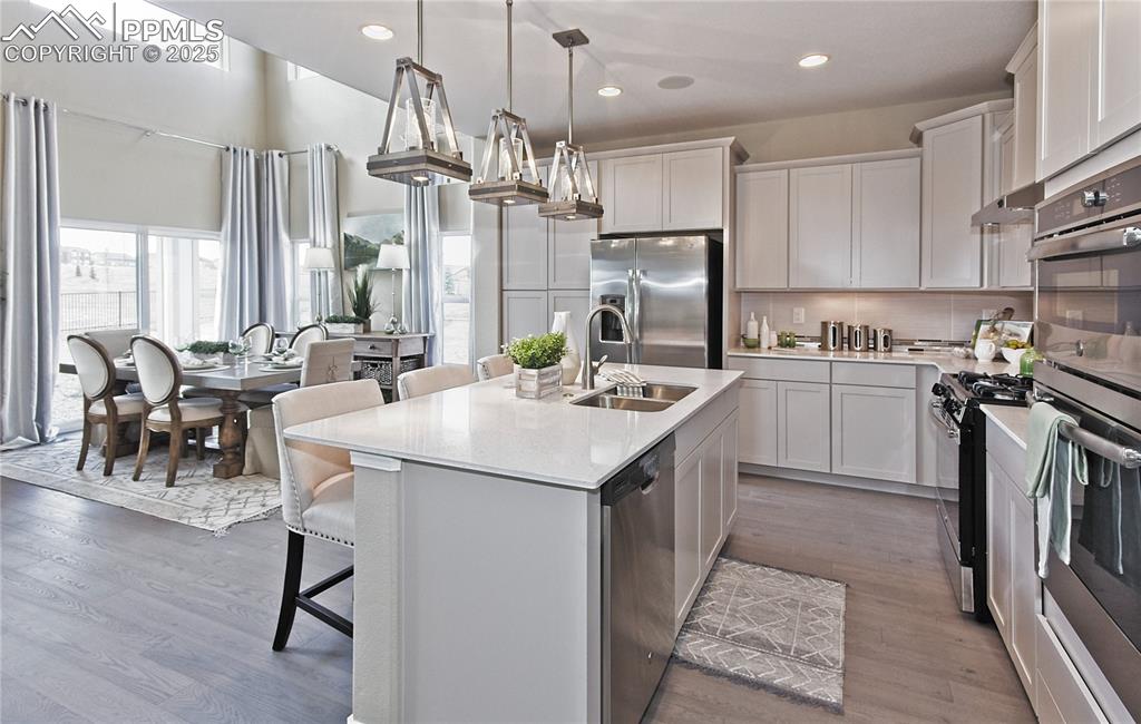 Kitchen featuring backsplash, a breakfast bar, stainless steel appliances, a kitchen island with sink, and recessed lighting