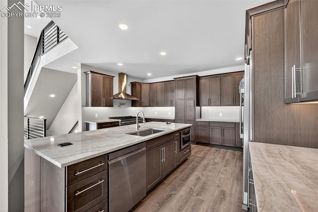 Kitchen with light stone counters, dishwasher, light wood-style floors, wall chimney exhaust hood, and recessed lighting