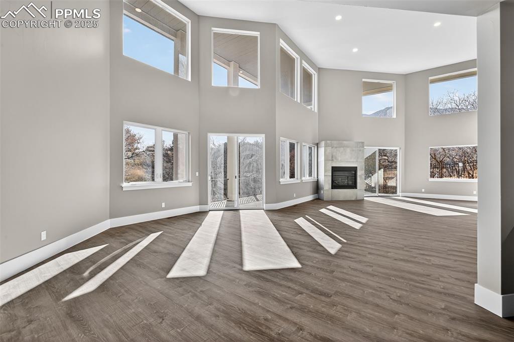 Unfurnished living room with a glass covered fireplace, dark wood-style floors, healthy amount of natural light, a towering ceiling, and recessed lighting