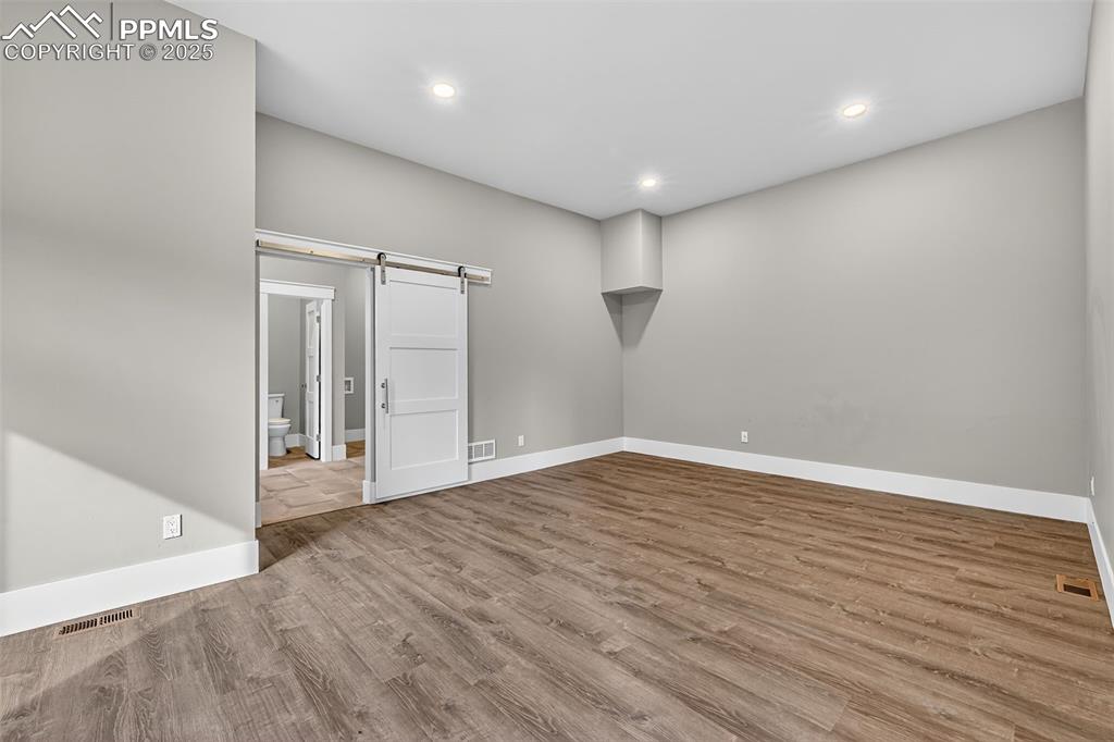 Empty room with a barn door, light wood-style floors, and recessed lighting
