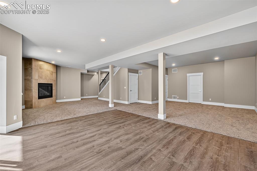 Below grade area featuring a tiled fireplace, stairs, light wood-style floors, recessed lighting, and light carpet