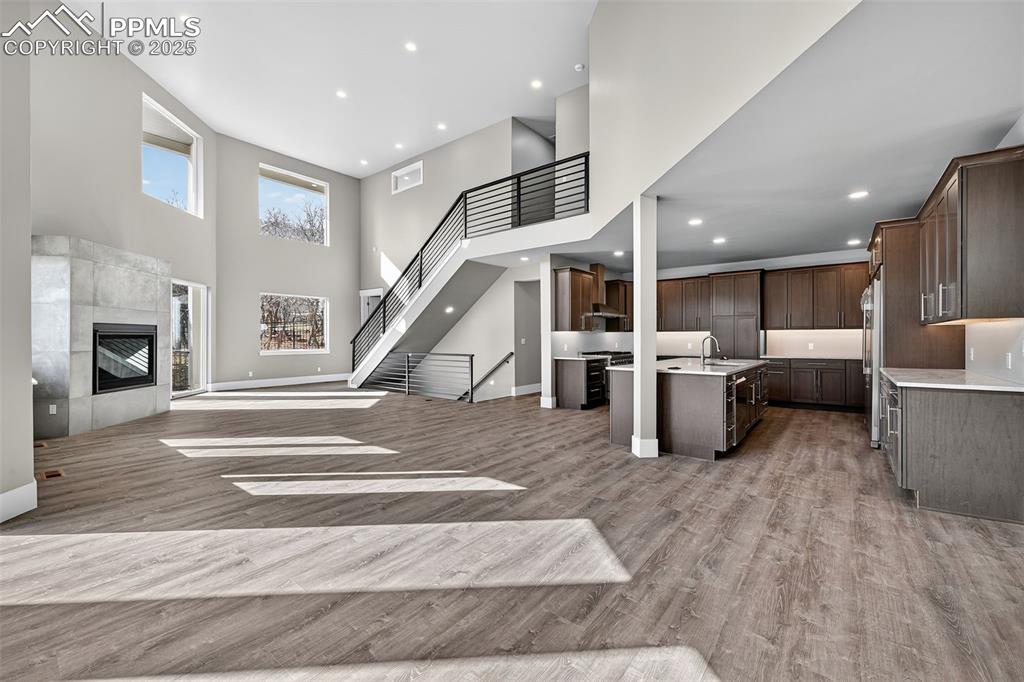 Unfurnished living room featuring a high ceiling, stairway, a tiled fireplace, recessed lighting, and light wood finished floors