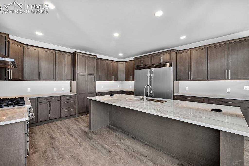 Kitchen with recessed lighting, light stone counters, dark brown cabinetry, appliances with stainless steel finishes, and light wood-type flooring