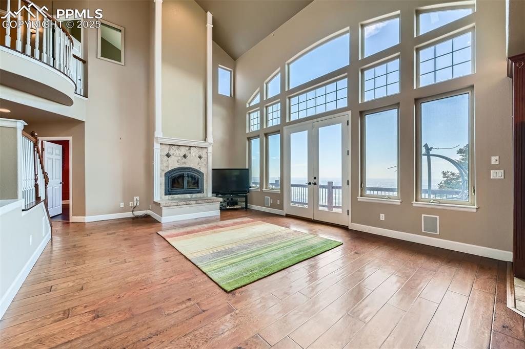 Unfurnished living room with high vaulted ceiling, hardwood / wood-style flooring, French doors, and a custom fireplace