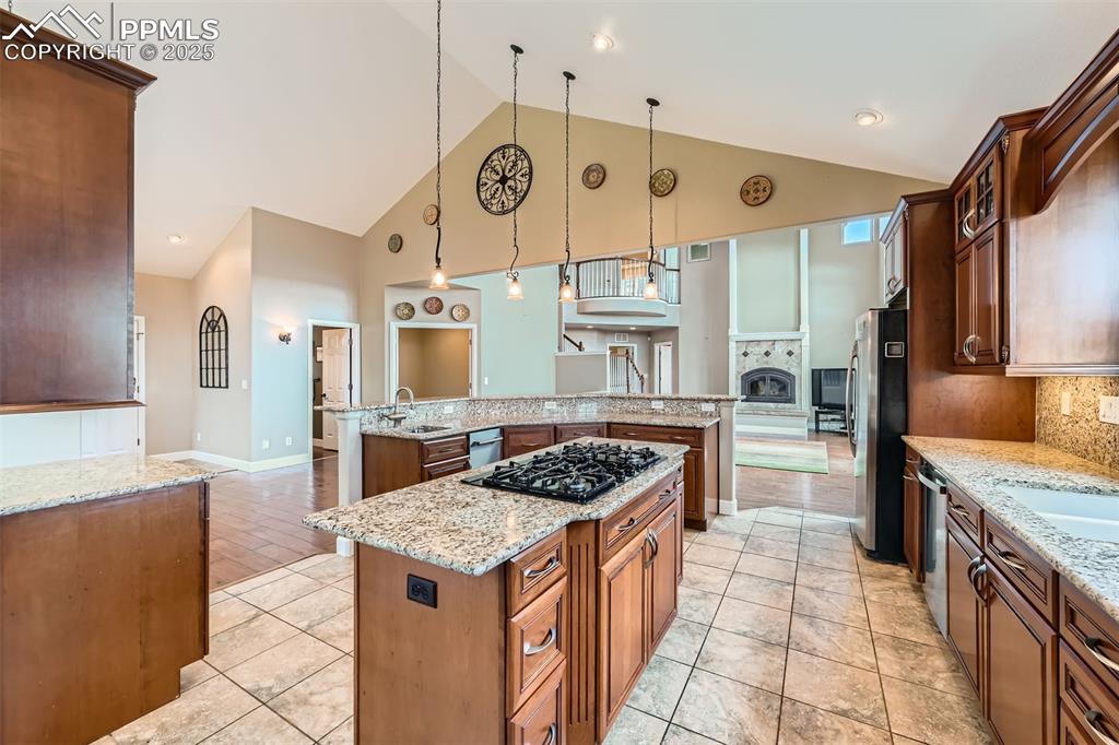 Kitchen with a large island with sink, high vaulted ceiling, decorative backsplash, appliances with stainless steel finishes, and hanging light fixtures