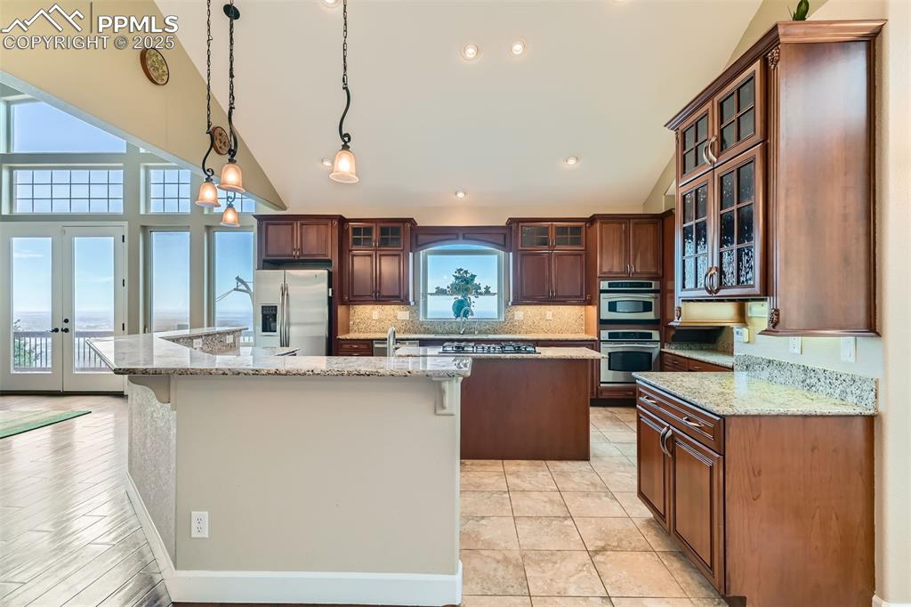 Kitchen with a spacious island, stainless steel appliances, vaulted ceiling, decorative backsplash, and French doors in the Great Room