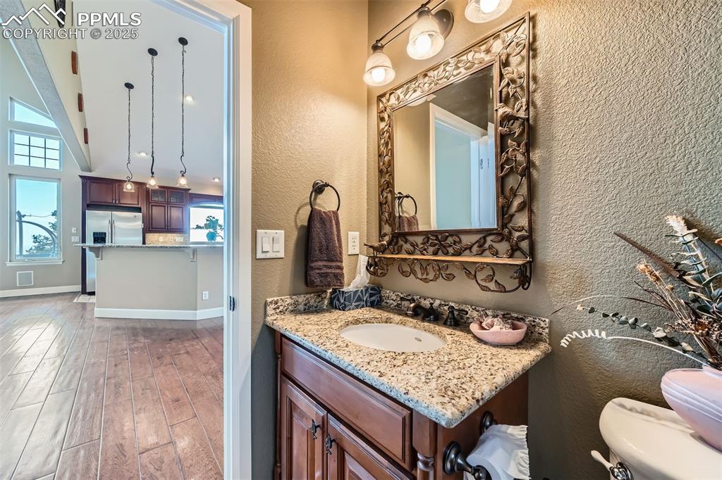 Half-bathroom with a textured wall, vanity with granite top, wood finished floors, and high ceiling