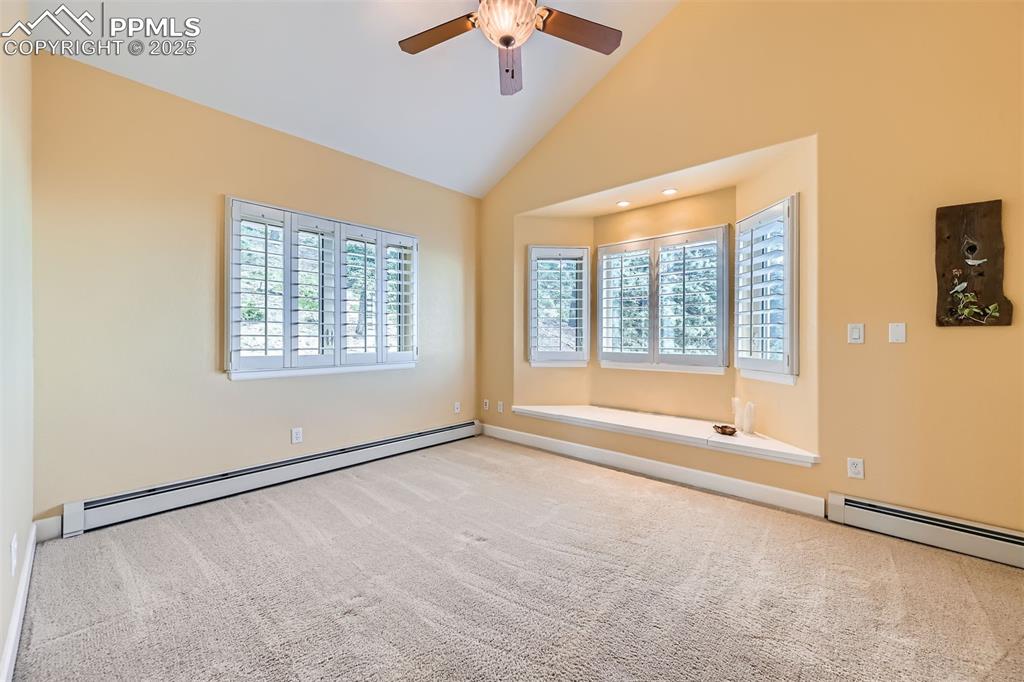 Carpeted bedroom with a window seat, custom blinds, a ceiling fan, and high vaulted ceiling