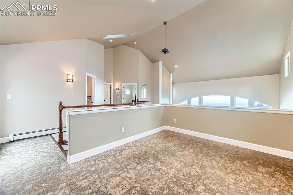 Loft area that exits to rear of home, complete with cork floors, a skylight, baseboard heating, and high vaulted ceiling