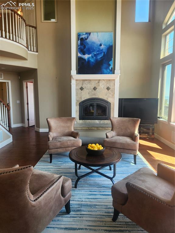 Living area featuring a towering ceiling, a tiled fireplace, wood finished floors, and stairway