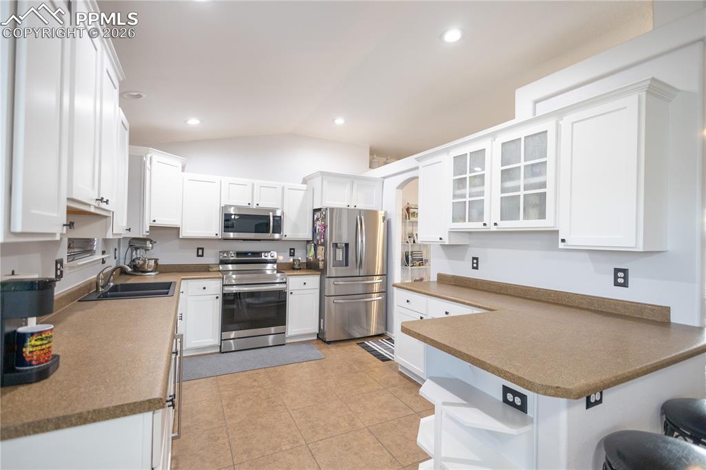 Kitchen featuring white cabinets, beverage cooler, a ceiling fan, vaulted ceiling, and decorative light fixtures