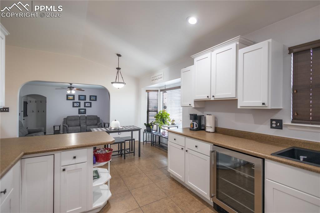 Kitchen featuring white cabinets, beverage cooler, a ceiling fan, vaulted ceiling, and decorative light fixtures