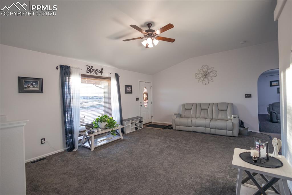 Living room with a ceiling fan, carpet flooring, vaulted ceiling, and arched walkways