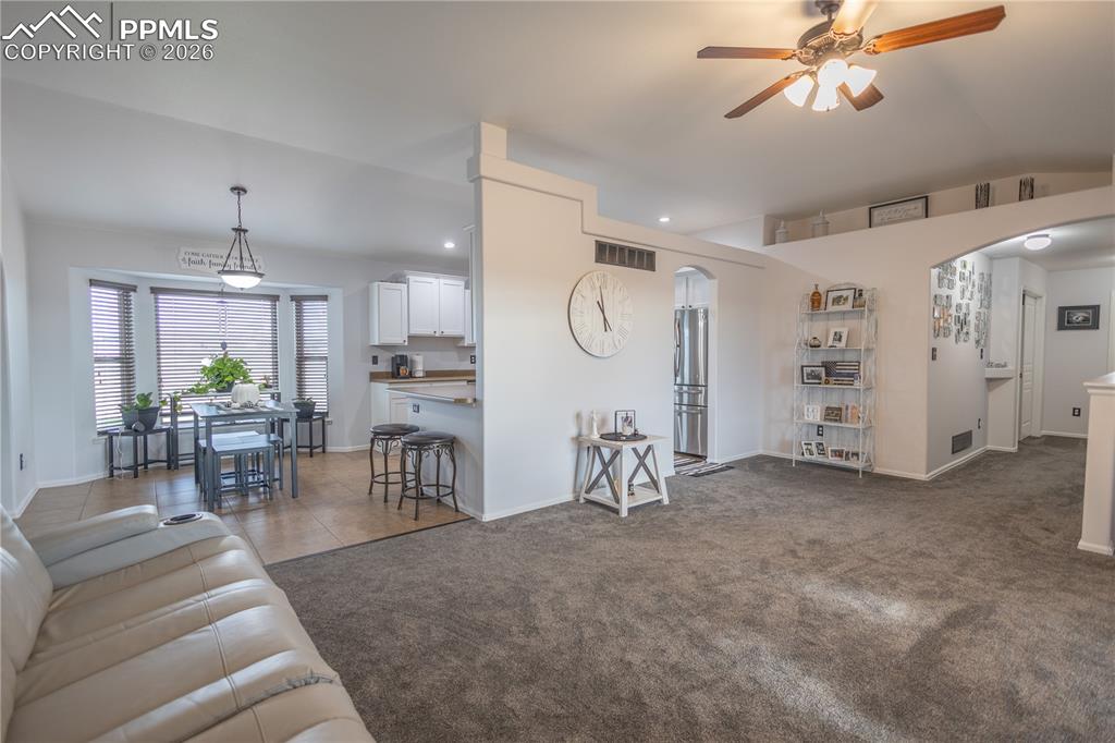 Living room featuring ceiling fan, arched walkways, recessed lighting, dark colored carpet, and dark tile patterned flooring