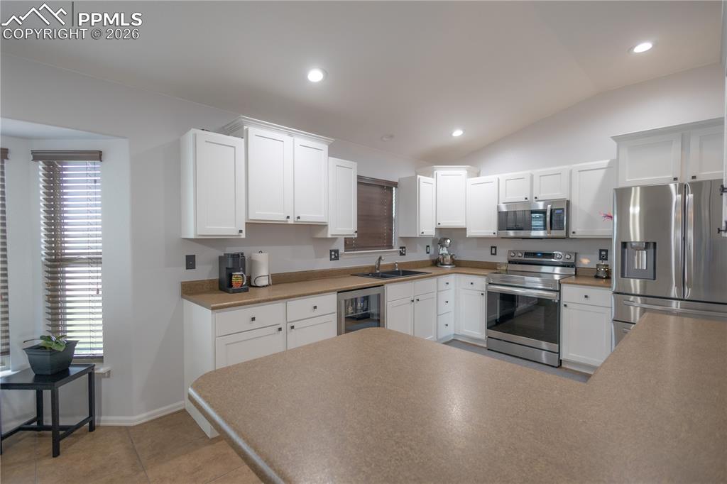 Kitchen featuring appliances with stainless steel finishes, white cabinets, vaulted ceiling, and recessed lighting