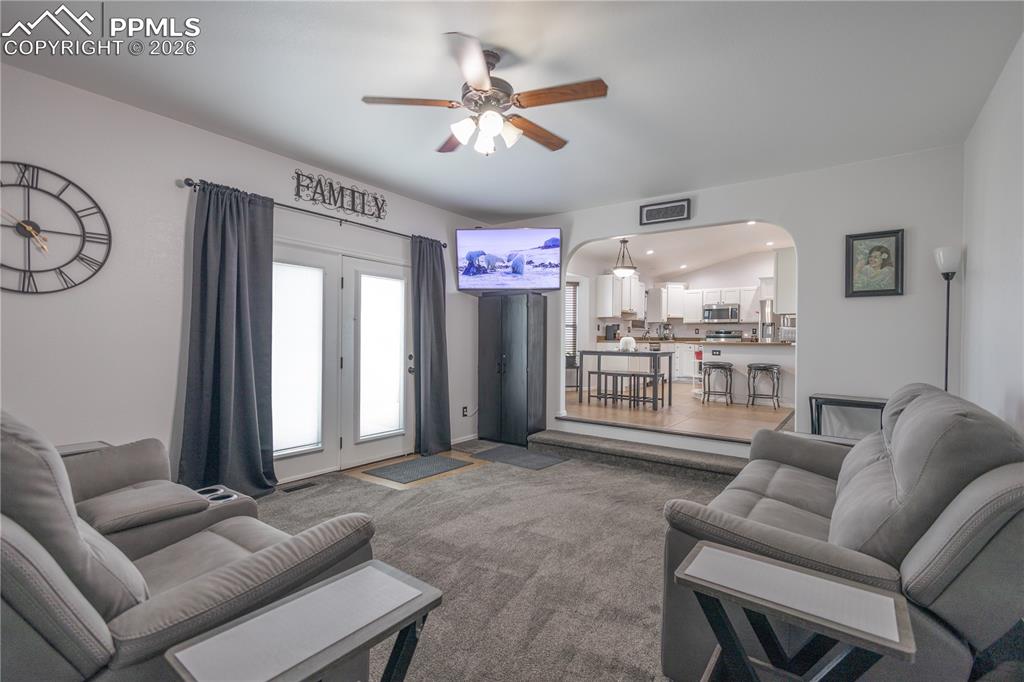 Carpeted living room featuring arched walkways, ceiling fan, and recessed lighting