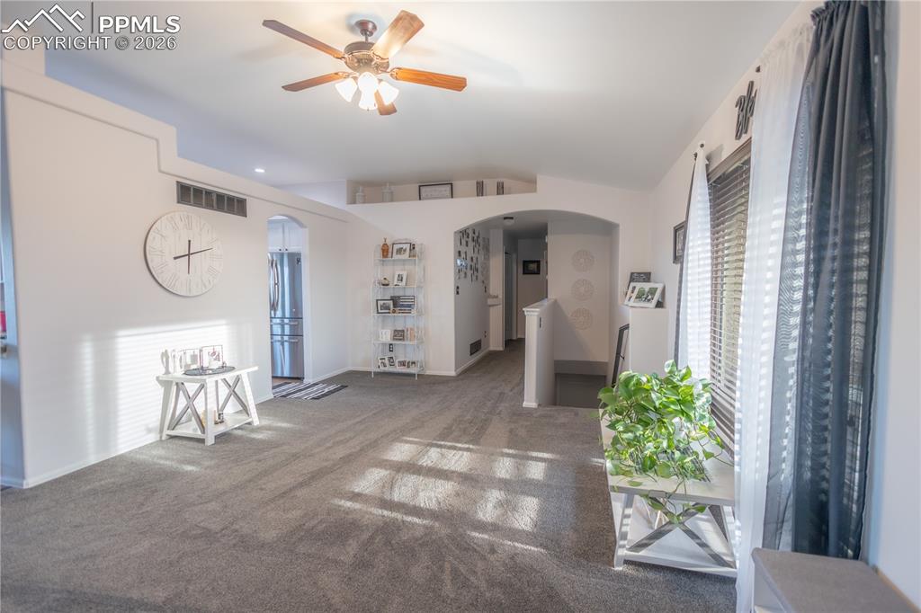 Carpeted living room featuring vaulted ceiling, arched walkways, and a ceiling fan