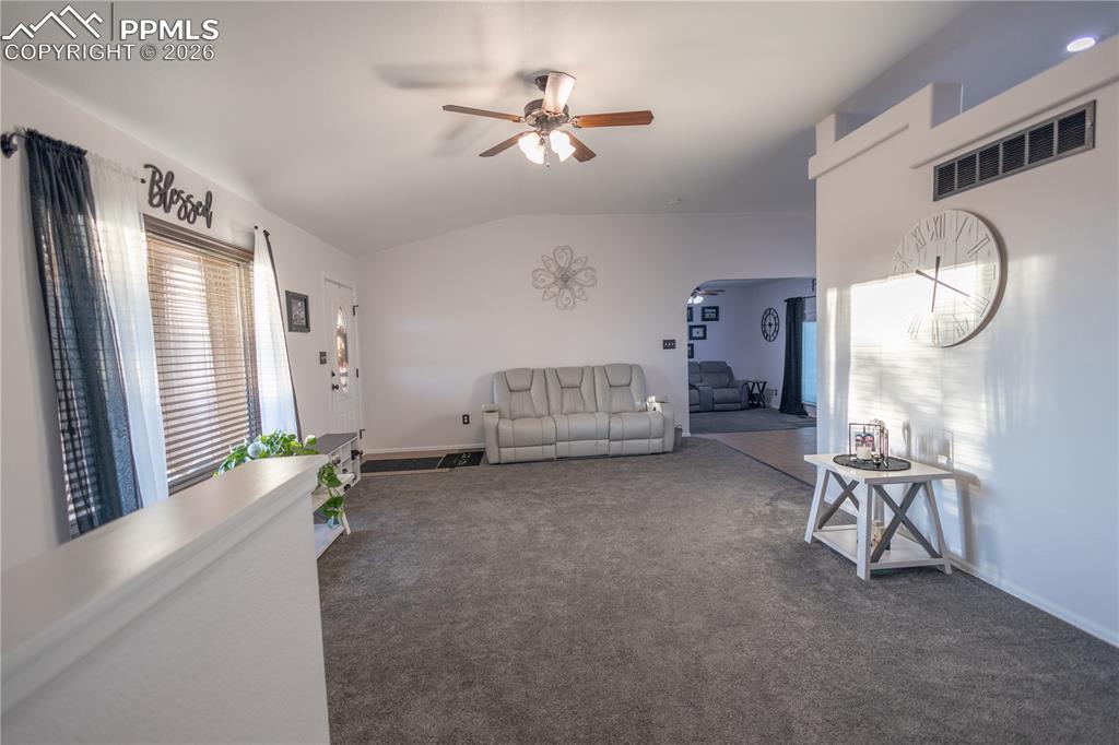 Carpeted living room with lofted ceiling and ceiling fan