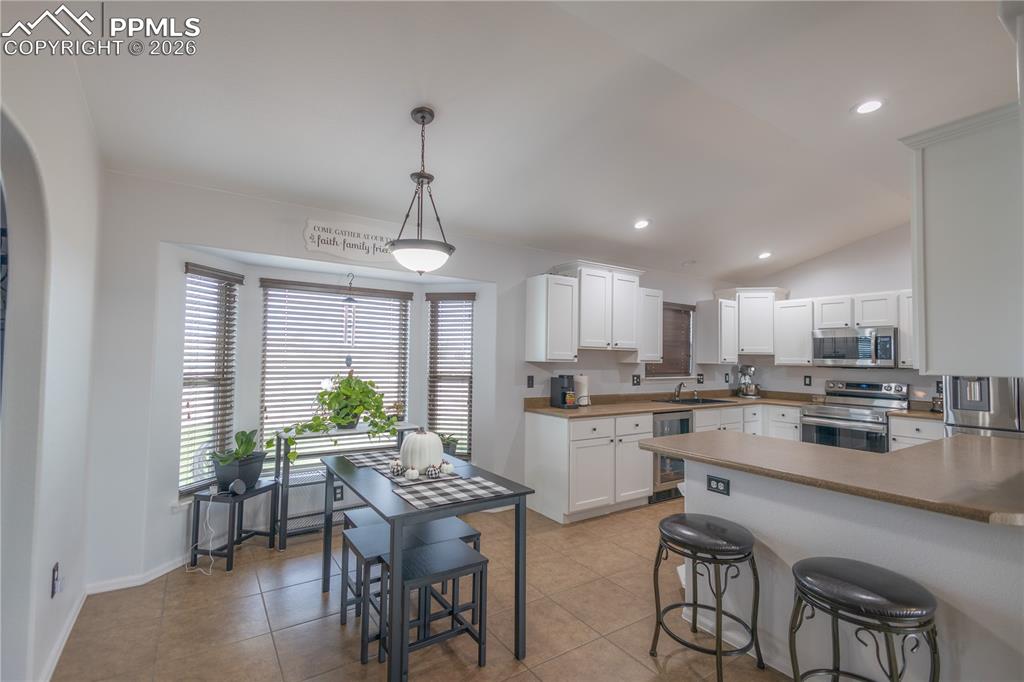Kitchen with white cabinets, glass insert cabinets, vaulted ceiling, stainless steel appliances, and open shelves