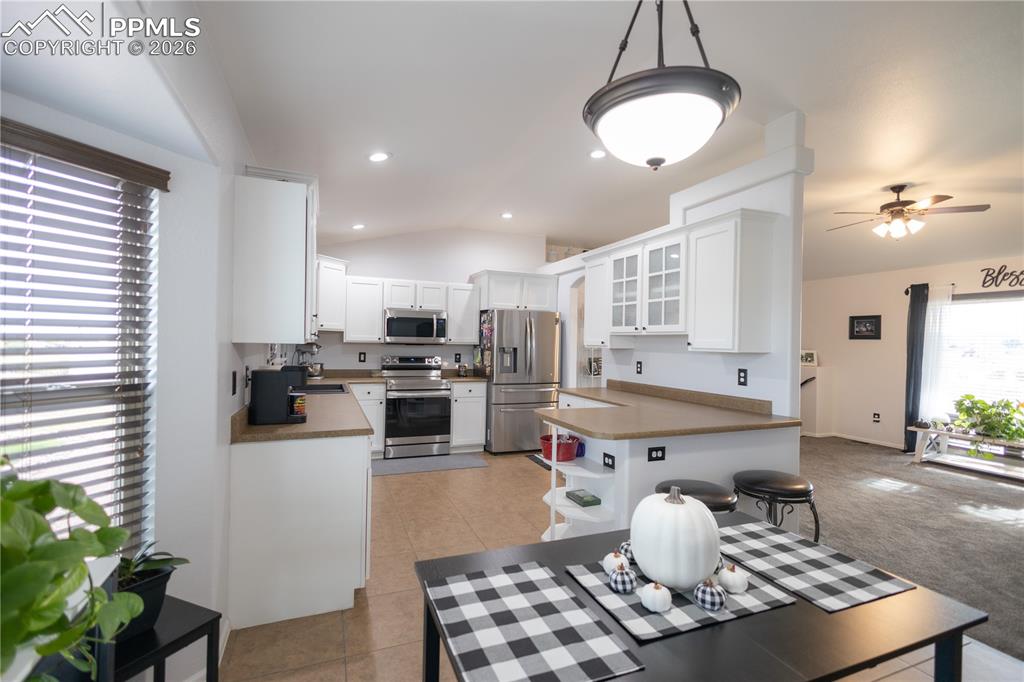 Kitchen with vaulted ceiling, dark countertops, white cabinetry, appliances with stainless steel finishes, and recessed lighting