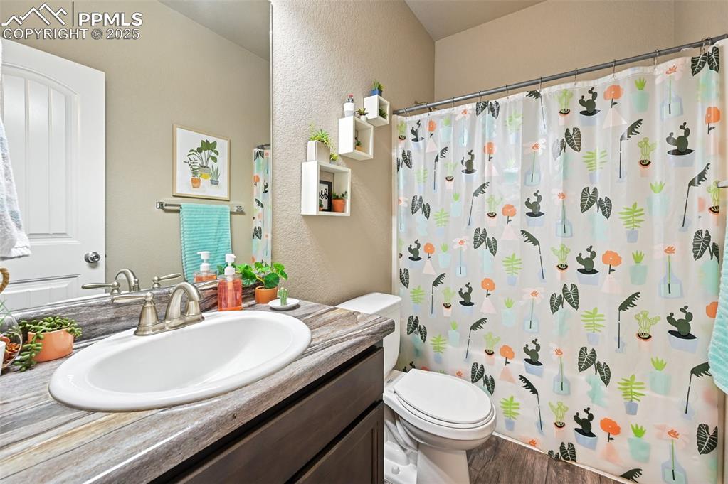 Full bathroom featuring vanity, a textured wall, a shower with shower curtain, and wood finished floors