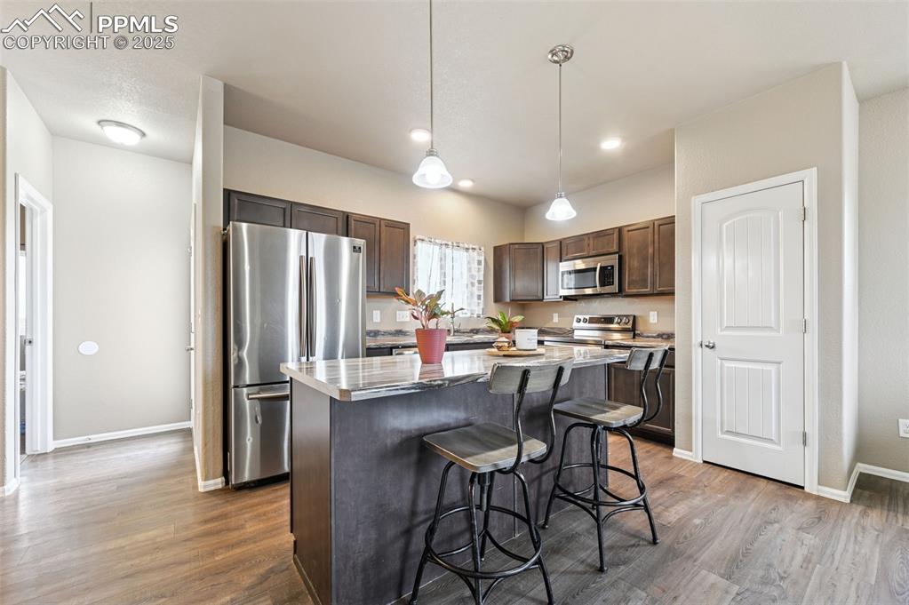 Kitchen with dark brown cabinets, appliances with stainless steel finishes, a kitchen bar, decorative light fixtures, and a kitchen island